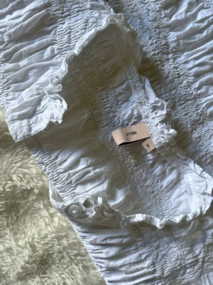 Vit smockad blus från Nelly - Säljer en vit blus från Nelly med smockade detaljer och volangkant vid halsen. Jag väljer att sälja denna därför att jag tycker den är för liten för mig. Använd ett fåtal gånger. Mycket fin och bekväm både till skolan, fest eller bara iväg under dagen! 