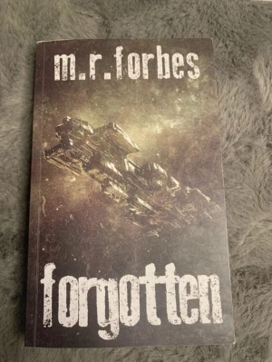 Forgotten av M.R. Forbes - Science fiction-roman med ett mörkt, rymdinspirerat omslag som visar ett stort rymdskepp mot en stjärnig bakgrund. Boken har mjukt omslag och titeln är tryckt i stora, vita bokstäver. Perfekt för dig som gillar äventyr i rymden.