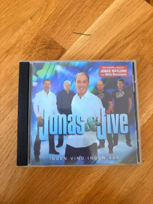 CD Jonas & Jive - Ingen Vind Ingen Väg - CD-skiva med albumet 'Ingen Vind Ingen Väg' av Jonas & Jive. Omslaget är färgglatt med bandmedlemmarna på framsidan. På baksidan finns en låtlista med 13 spår, bland annat 'Kan Jag Hjälpa Att Jag älskar Dig ännu' och 'Mississippi'. Perfekt för dig som gillar dansband. Ej orginal skiva!