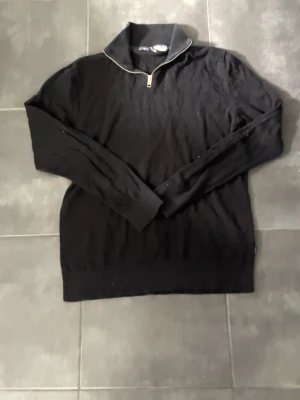 Svart tröja med halv dragkedja Jack & Jones - Klassisk svart tröja från Jack & Jones med halv dragkedja vid kragen. Långärmad modell i mjukt material, perfekt för lager på lager. Enkel och stilren design som passar till det mesta.