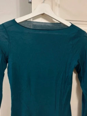 Mörkgrön långärmad topp - Klippt i ärmen därefter priset En enkel och stilren mörkgrön långärmad topp med rund halsringning. Perfekt att matcha med jeans eller kjol för en clean look. Tunt och mjukt material som känns skönt mot huden.