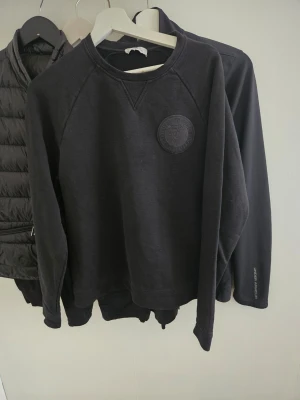 Svart sweatshirt från vrsache - En stilren orginal svart sweatshirt med rund hals och ett diskret tygmärke på bröstet. 