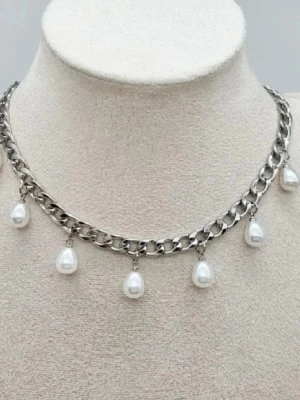 Kedjehalsband med droppformade pärlor - Snyggt halsband i silverfärgad metall med grov kedja och hängande droppformade vita pärlor. Perfekt för att ge din outfit en trendig och elegant touch. Låset är klassiskt och halsbandet har en modern vibe.
