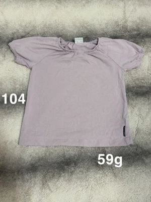 Ljuslila kortärmad topp - Söt ljuslila topp med korta puffärmar och rund hals. perfekt för en avslappnad och bekväm stil. Enkel design utan mönster eller tryck, vilket gör den lätt att matcha med olika outfits.🌸 Fint använt skick. Storlek 104