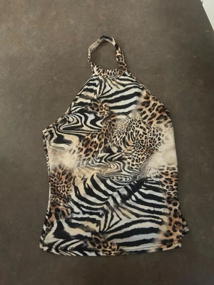 Halterneck topp med leopard- och zebramönster - Säljer en snygg halterneck topp med både leopard- och zebramönster i beige, svart och bruna toner. Toppen är ärmlös och har en smal passform som ger en trendig look. Perfekt för dig som vill sticka ut med djurmönster!