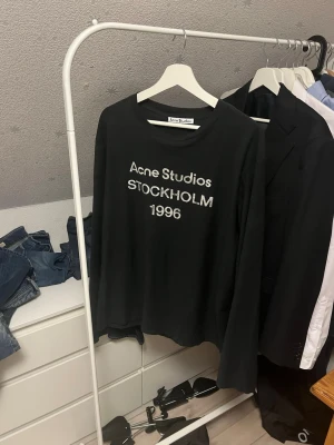 Svart Acne Studios longsleeve tröja - Svart långärmad topp från Acne Studios med tryck 'Acne Studios STOCKHOLM 1996' framtill. Klassisk rund halsringning och relaxed fit. Perfekt till jeans eller kjol för en clean och stilren look. Tröjan är i M skriv vid funderingar!