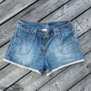 Vintage shorts med spets  - Superfina vintage jeansshorts med spets och rosa sömmar från märket Next. Midjemått: 36cm, längd: 27cm! 