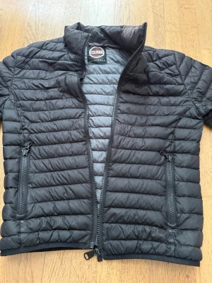 Svart dunjacka från Colmar - Snygg svart dunjacka från Colmar med quiltad design och hög krage. Jackan har två dragkedjeförsedda fickor framtill och hel dragkedja. Perfekt för kalla vinterdagar och riktigt lätt att bära. Klassisk och stilren look som passar till det mesta.