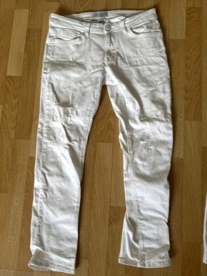 Vita snygga jeans med slitningar - Säljer ett par vita slim fit jeans med snygga slitningar på låren och knäna. Perfekta för en trendig och avslappnad look.
