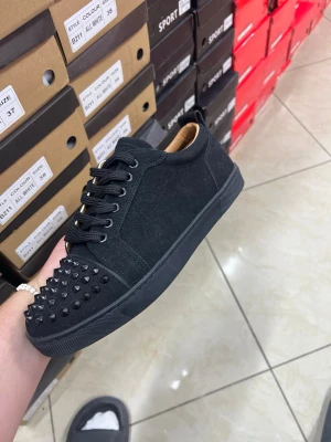 Svarta sneakers med nitar och röd sula - Snygga svarta sneakers med mattsvart ovandel i mockaliknande material och coola svarta nitar på tån. Skon har en klassisk låg profil och en ikonisk röd sula som sticker ut. Perfekt för dig som vill ha något extra till din streetwear-look.