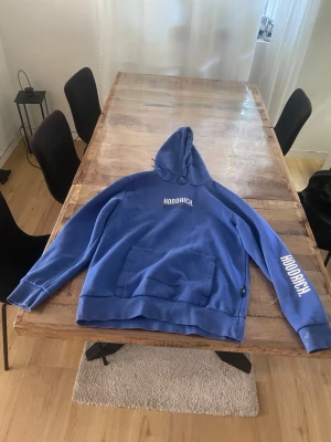 Blå hoodie från Hoodrich med tryck - Snygg blå hoodie från Hoodrich med vit logga på bröstet och ärmen. Har stor känguruficka och texten 'FROM NOTHING TO SOMETHING' tryckt nedanför fickan. Klassisk huva och ribbade muddar. Perfekt för en chill och street-inspirerad stil. Storleken är S men passar även M. Pris går och diskuteras men även byte går!