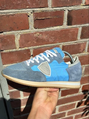 Phillips model sneaker  - Snygga sneakers i blått och grått med vita skosnören och beige sula. Skon har en mix av mocka och textilmaterial samt en tydlig logga på sidan. Perfekt för dig som gillar en stilren men sportig look.