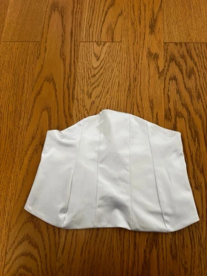 Vit satinliknande korsett med snörning - Snygg vit korsett i satinliknande material med stilrena sömmar framtill och snörning baktill för justerbar passform. Perfekt för att skapa en trendig och elegant look.