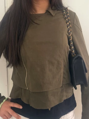 Olivgrön skinnjacka med dragkedjor accepterar bud 💕 - Snygg olivgrön skinnjacka med asymmetrisk dragkedja framtill och dragkedjor vid ärmsluten. Jackan har en modern krage och raka linjer som ger en cool look. Perfekt för dig som vill ha en stilren och trendig jacka till din outfit.