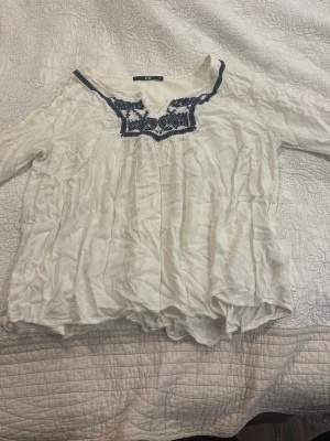 Vit blus med blå brodyr från LTB - Säljer en luftig vit blus från LTB med långärmad design och snygg blå brodyr runt ringningen. Blusen har en avslappnad passform och är gjord i ett tunt, skönt tyg som ger en bohemisk känsla.