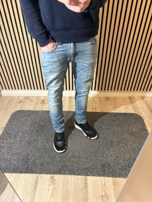 Nudie Jeans - Säljer ett par ljusblå slim fit Nudie Jeans med klassisk femficksmodell och normal midja. Jeansen har en snygg tvätt med lätt slitning och smal passform hela vägen ner. Perfekta till sneakers och hoodie för en avslappnad look.