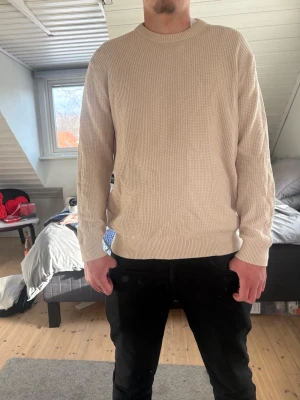Stickad tröja  - Beige stickad tröja från Kappahl i storlek L. Klassisk modell med rund hals och strukturerad stickning som ger ett stilrent och modernt uttryck. Rak passform som sitter snyggt och bekvämt.  En mångsidig tröja som passar perfekt till både jeans och mer uppklädda outfits. Perfekt basplagg för höst, vinter och svala vårdagar. I fint skick.
