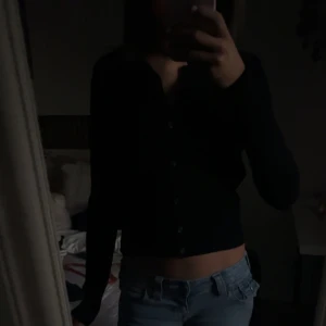 Svart kofta från H&M - En svart, croppad kofta från H&M med långa ärmar och knappar framtill. Perfekt att slänga över en t-shirt eller bära som den är. Enkel och stilren design som passar till jeans eller kjol.