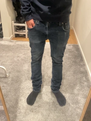 Mörkblå nudie jeans - Säljer ett par mörkblå slim fit jeans med lätt slitning och klassisk femficksmodell. Jeansen har normal midja och smala ben, perfekta för en clean och modern look. Materialet är mjukt denim som sitter skönt hela dagen.
