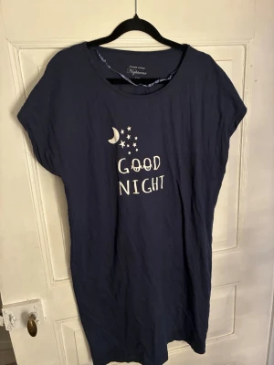 Mörkblå nattlinne från Mywear Woman - Mörkblått nattlinne från Mywear Woman med tryck av måne, stjärnor och texten 'Good Night' framtill. Kortärmad modell med rund halsringning, tillverkat i mjukt bomullsmaterial för extra komfort. Perfekt för mysiga kvällar och nätter.