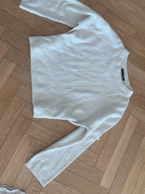 Vit stickad tröja  - Klassisk vit stickad tröja med rund halsringning och långa ärmar. Tröjan har en enkel och stilren design med ribbade muddar vid ärmslut och nederkant. Perfekt att matcha med jeans eller kjol för en clean look.