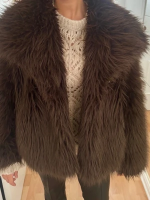 Mörkbrun fluffig pälsjacka - Säljer en mörkbrun, superfluffig pälsjacka med bred krage och oversized passform. Jackan har långa ärmar och är gjord i fuskpäls som känns mjuk och varm. Perfekt för kalla dagar när du vill sticka ut och hålla dig varm. (Kolla sista bilden) går att fixa