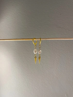 Guldörhängen med pärlor och spikes - Säljer ett par trendiga örhängen i guldton med vita pärlor och coola guldfärgade spikes. Örhängena har en modern design med hjärtformad ögla och hängande detaljer. Perfekta för dig som vill sticka ut med din stil . Egengjorda 
