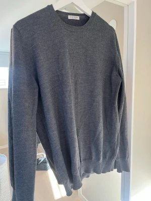 Mörkgrå stickad tröja Gran Sasso - Klassisk mörkgrå stickad tröja från Gran Sasso med rund halsringning och ribbade muddar vid ärmslut och nederkant. Tröjan har en enkel och stilren design, perfekt för lager på lager och passar till det mesta. Merino.