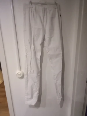 Vita slim byxor från LauRie - Säljer ett par vita slim byxor från LauRie, modell Sanna. De har en elastisk midja och smal passform som sitter snyggt längs benen. Perfekta för dig som gillar en clean och enkel stil. Materialet känns mjukt och stretchigt för extra komfort.