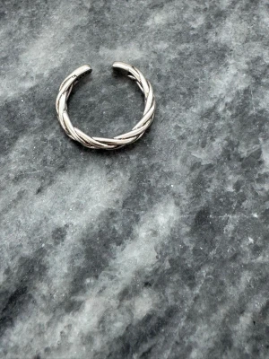 Flätad silverring i äkta 925 silver - Snygg och stilren ring i äkta 925 silver med flätad design. Är framförallt till för lillfingret men ringen är öppen baktill vilket gör den justerbar och enkel att bära på olika fingrar. 