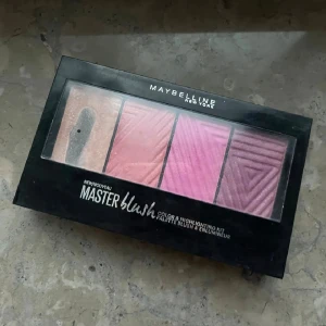 Maybelline Master Blush palett - Master Blush palett från Maybelline med fyra nyanser: en skimrig highlighter i champagne, en persikorosa, en kall rosa och en mörkare bärig rosa. Pudret har pressad form med geometriskt mönster och kommer i en svart plastförpackning med spegel.