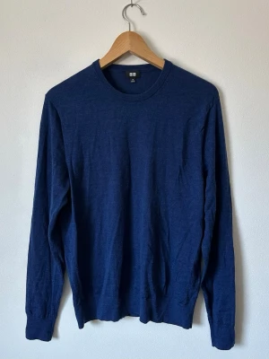 Mörkblå stickad tröja från Uniqlo - En stilren mörkblå stickad tröja från Uniqlo med rund halsringning och långa ärmar. Tröjan har en klassisk passform och är tillverkad i ett mjukt, tunt stickat material som passar perfekt till lager-på-lager-stil. 8D27