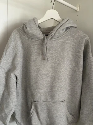 Grå hoodie från Bik Bok - Klassisk grå hoodie från Bik Bok med huva och känguruficka framtill. Tillverkad i mjukt sweatshirtmaterial som är perfekt för chill dagar. Dragsko i huvan och avslappnad passform gör den extra bekväm.