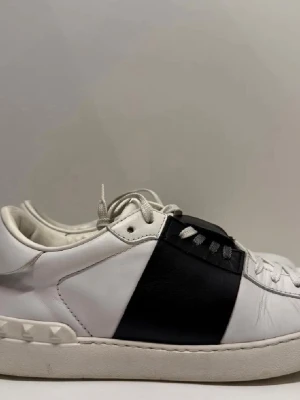 Valentino open - Snygga sneakers från Valentino i vitt läder med en bred svart läderpanel över mitten. Skorna har vita snören och coola nitar på hälen. Perfekt för dig som gillar stilrena men ändå unika detaljer.