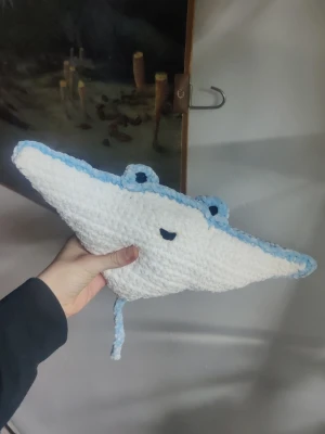 Virkad stingrocka mjukisdjur - Handgjord virkad stingrocka i vitt och ljusblått garn. Den har ett gulligt ansikte med broderade ögon och mun, samt en lång svans. Perfekt som dekoration eller mysig kompis till sängen. Gjord av mjukt garn och har en unik form som liknar en stingrocka.