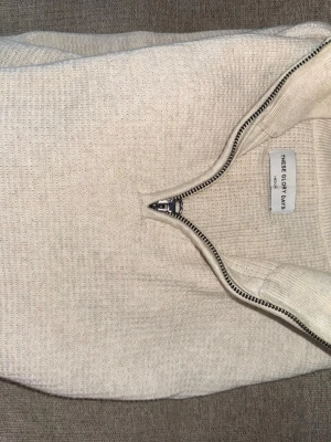 Beige stickad halvzip från These Glory Days - Stickad tröja i beige från These Glory Days med halvzip och hög krage. Tröjan har en diskret struktur i materialet och långa ärmar. Perfekt för lager på lager och enkel att matcha med olika outfits.