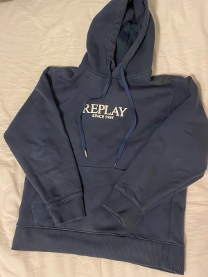 Mörkblå hoodie från Replay - Blå hoodie från replay med replay ligga på bröstet. Storlek S. Mycket bra skick förutom att den saknar en metall bit på ena snöret. Nypris:1300kr