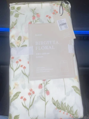 Birgitta Floral påslakanset 230x220 cm - Säljer ett helt nytt oanvänd  Birgitta Floral påslakanset i satin, 230x220 cm. Setet är i 100% bomull och har ett blommigt mönster i grönt, rosa och vitt. Innehåller två örngott och ett påslakan. Perfekt för dig som gillar mjuka och svala material med romantisk känsla.