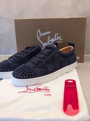 Mörkblå Christian Louboutin sneakers - Snygga mörkblå sneakers från Christian Louboutin i mocka med coola svarta nitar på tån. Skorna har vita sulor, svarta skosnören och en klassisk låg modell. Perfekta för dig som vill sticka ut med en lyxig och edgy stil.