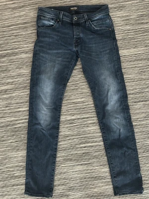 Mörkblå slim fit jeans - Snygga mörkblå slim fit jeans med lätt slitning på låren och klassiska fem fickor. Jeansen har en rak passform och stängs med dragkedja och knapp. Perfekta till vardagslooken och passar till det mesta.