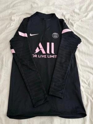 Svart PSG träningströja från Nike - Svart långärmad träningströja från Nike med Paris Saint-Germain-logga och rosa detaljer. Bra skick och inga problem med den. 