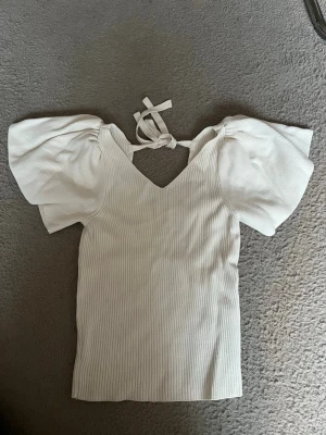 Vit ribbad topp med puffärm och knyt - TRYCK EJ KÖP DIREKT!!💗Superfin vit ribbad topp med v-ringning, puffärmar och knyt i nacken. Toppen har en figurnära passform och är perfekt för dig som gillar trendiga detaljer och en feminin look. Hör av dig vid intresse💗