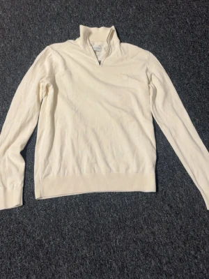 Vit stickad tröja med dragkedja - Snygg vit stickad tröja från These Glory Days med halv dragkedja i halsen. Tröjan har långa ärmar, ribbade muddar och en stilren design som passar perfekt till många outfits.