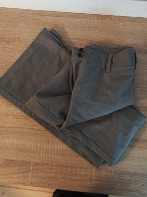 Grå kostymbyxor bootcut ( INSYDDA ) - Snygga grå kostymbyxor med klassisk tight passform. Byxorna har hällor för bälte, två knappar i midjan. Perfekta för en stilren look. Materialet känns mjukt och har en lätt struktur. ( Dom är insydda från en M till en xs/xxs )