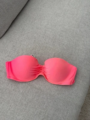 Neonrosa bandeau bikiniöverdel - Säljer en snygg bandeau bikiniöverdel i neonrosa färg från Victoria secret. Modellen är axelbandslös med lätt rynk framtill för en schysst passform, storlek 36B. Aldrig använd. 