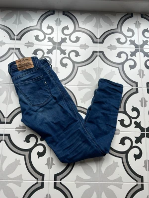 Blå jeans från Replay - Snygga blå jeans från Replay med klassisk femficksdesign och raka ben. Jeansen har en mörk tvätt och detaljerade sömmar, samt Replay-logga på fickan och bak på linningen. Perfekta för en trendig och avslappnad stil.