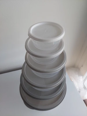 Set med runda plastburkar med lock - Sex genomskinliga runda plastburkar i olika storlekar med vita lock. Perfekta för att förvara mat, snacks eller småsaker. Burkarna är stapelbara och smidiga att ha i köket eller ta med på picknick.