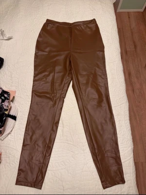 Bruna faux leather leggings SHEIN - Snygga bruna leggings i fuskläder från SHEIN, storlek M (EU 38). De har hög midja och smal passform som ger en trendig look. Materialet är glansigt och stretchigt för extra komfort. Helt nya✨