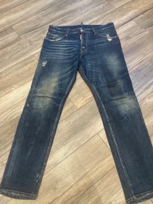 Mörkblå slitna jeans med raka ben - Säljer ett par mörkblå jeans med raka ben och snygga slitningar på låren och knäna. Jeansen har klassisk femficksdesign och tydliga tvättade detaljer för en cool, avslappnad look. Perfekta för dig som gillar streetstyle och en trendig vibe.
