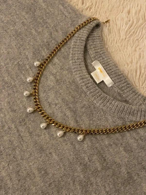 Guldfärgat halsband med pärlor - Snyggt halsband iguldfärgad rostfritt med kedja och vita pärlor som hänger längs hela halsbandet. Perfekt för att ge din outfit en cool och elegant touch. Passar dig som gillar trendiga accessoarer och vill sticka ut.